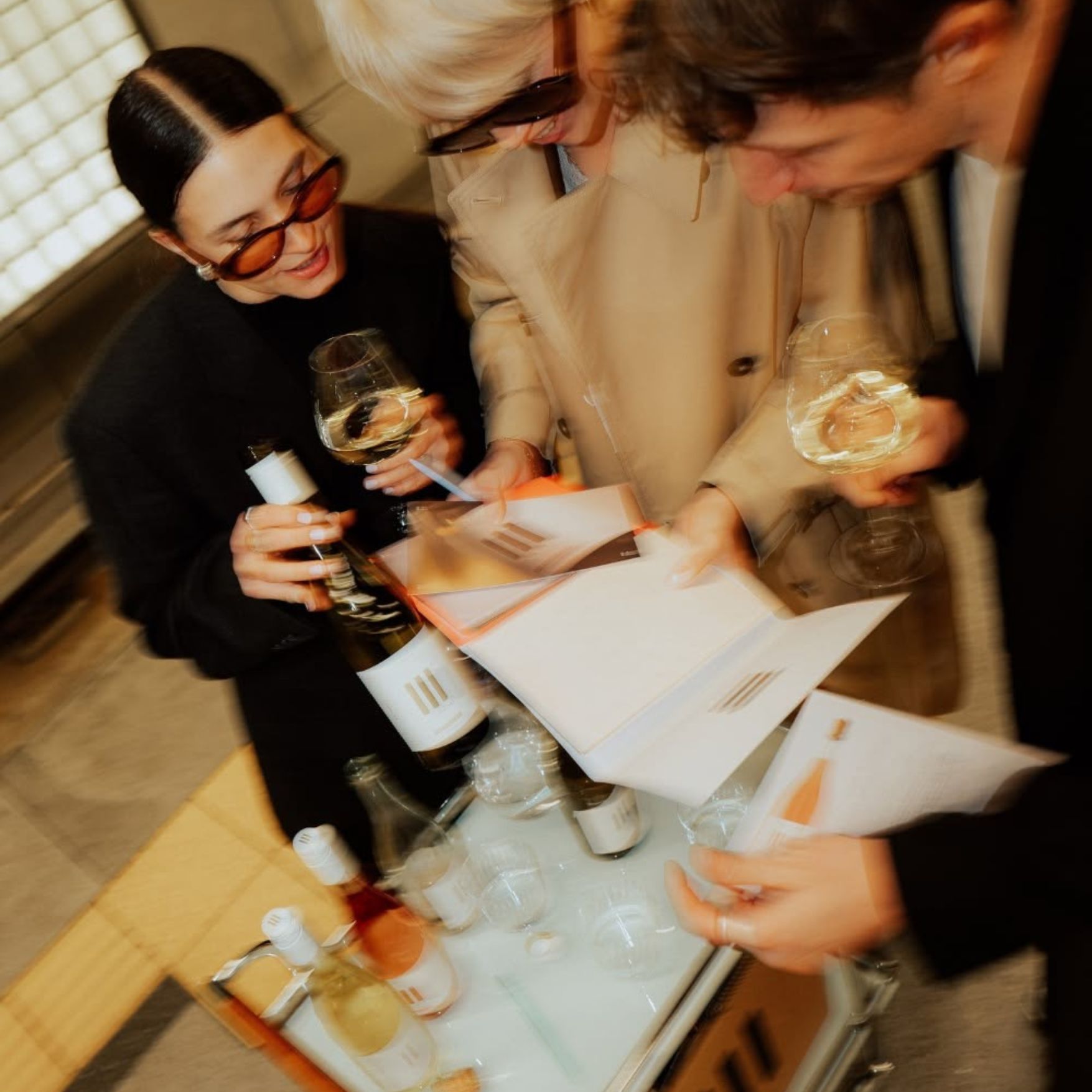Drei Gäste schauen gemeinsam auf eine Weinkarte und Weinflaschen